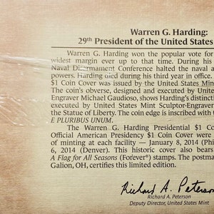 May include: A close-up of a commemorative coin cover featuring Warren G. Harding, the 29th President of the United States. The cover includes two gold-colored coins, one depicting Harding's portrait and the other the Statue of Liberty. The text on the cover reads "Warren G. Harding: 29th President of the United States of America".