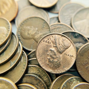 K&ouml;nnte beinhalten: Nahaufnahme eines Stapels kupferfarbener US-Pennys. Die M&uuml;nzen sind in einem zuf&auml;lligen Muster angeordnet, wobei sich einige M&uuml;nzen &uuml;berlappen. Die M&uuml;nzen sind alle in gutem Zustand, ohne sichtbare Sch&auml;den oder Abnutzung. Die M&uuml;nzen sind alle mit dem Jahr 1957 oder fr&uuml;her datiert. Der Text auf den M&uuml;nzen lautet "IN GOD WE TRUST" und "LIBERTY".