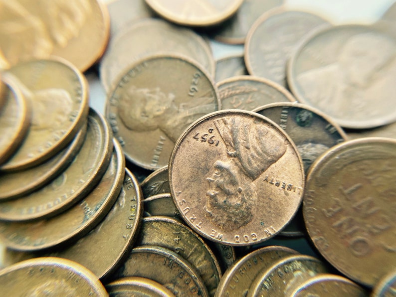 K&ouml;nnte beinhalten: Nahaufnahme eines Stapels kupferfarbener US-Pennys. Die M&uuml;nzen sind in einem zuf&auml;lligen Muster angeordnet, wobei sich einige M&uuml;nzen &uuml;berlappen. Die M&uuml;nzen sind alle in gutem Zustand, ohne sichtbare Sch&auml;den oder Abnutzung. Die M&uuml;nzen sind alle mit dem Jahr 1957 oder fr&uuml;her datiert. Der Text auf den M&uuml;nzen lautet "IN GOD WE TRUST" und "LIBERTY".