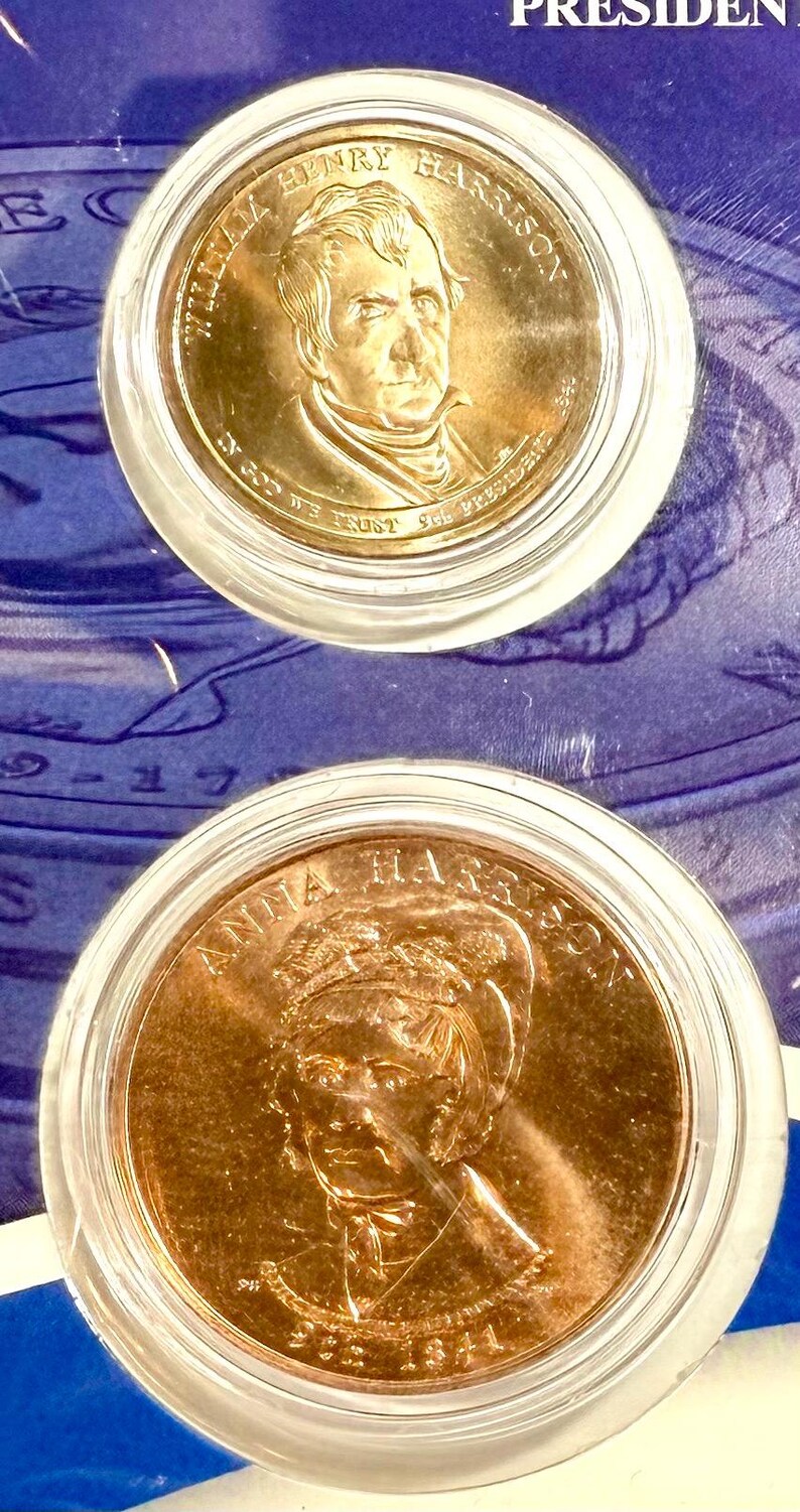 Pu&ograve; includere: Due monete color oro in custodie protettive. La moneta superiore presenta un ritratto di William Henry Harrison e il testo "WILLIAM HENRY HARRISON" e "IN GOD WE TRUST". La moneta inferiore mostra Anna Harrison.