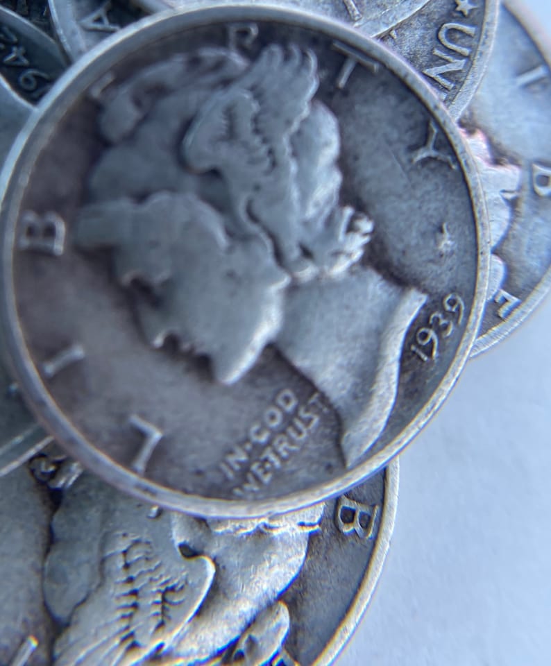 K&ouml;nnte beinhalten: Nahaufnahme eines Stapels Silberm&uuml;nzen mit der Aufschrift "In God We Trust" und dem Jahr "1939" auf der obersten M&uuml;nze.