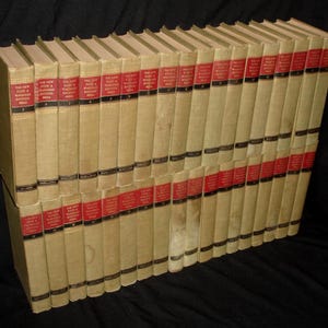 May include: A collection of vintage books with beige covers and red spines. The spines have black text and the title "The New Funk & Wagnalls Encyclopedia". The books are arranged in a diagonal row.