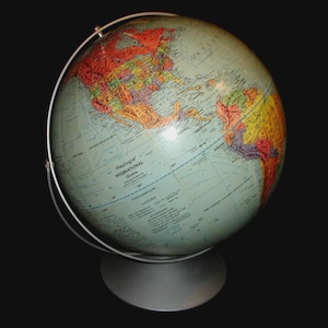 Może przedstawiać: Zabytkowy globus z kolorowymi kontynentami i jasnoniebieskim oceanem. Jest zamontowany na srebrnym metalowym stojaku i ma srebrny pierścień południka. Globus ma napis "Replogle International Globe".