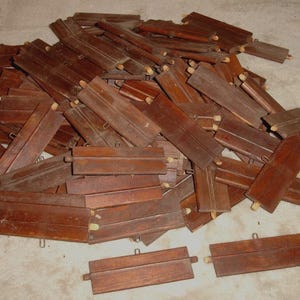 Peut inclure: Un tas de petites pièces de bois rectangulaires de couleur brun foncé. Chaque pièce a une forme rectangulaire avec une petite projection en forme de poignée à chaque extrémité. Le grain du bois est visible, et les pièces semblent être anciennes.