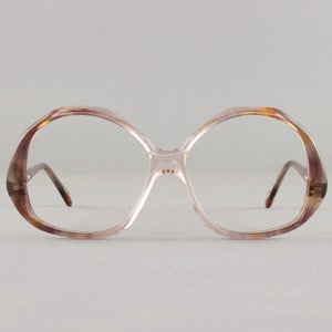 May include: Oversized, vintage-style eyeglasses with a light brown and pink gradient frame. The glasses have a large, rounded shape and thin, dark brown temples. The lenses are clear, and the bridge is a light pink color.