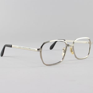 Op de afbeelding: Zilverkleurige metalen bril met een rechthoekig montuur en zwarte pootjes.