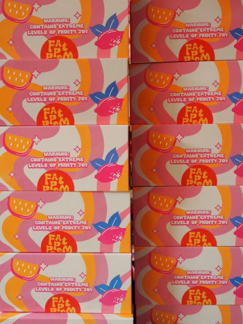 Puede incluir: Cajas apiladas con un dise&ntilde;o retro. Las cajas presentan rayas onduladas rosas, naranjas y blancas, ilustraciones de rodajas de lim&oacute;n y limones rosas. El texto en las cajas dice "WARNING: CONTAINS EXTREME LEVELS OF FRUITY JOY" y "FAT PLOM".