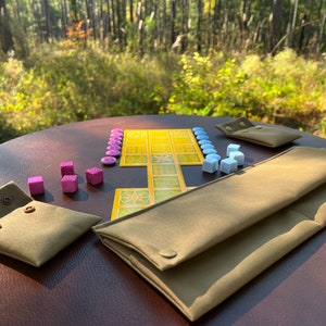 May include: A brown leather table with a yellow and green board game, pink and blue dice, and two brown canvas pouches with buttons.