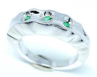 May include: A silver ring with a textured, organic design. The ring features three round, bright green gemstones set into the top. The band has a smooth, polished interior.