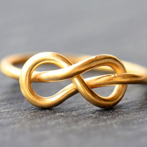 Op de afbeelding: Een gouden ring met een oneindigheidsknoop. De ring is gemaakt van glad, gepolijst metaal en heeft een eenvoudig, elegant ontwerp.
