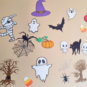 Peut inclure: Diverses découpes en papier sur le thème d'Halloween, comprenant des fantômes, des chauves-souris, des araignées, une momie, un chapeau de sorcière et une citrouille. Les découpes sont de couleurs variées, comme le noir, le blanc, l'orange et le violet, sur fond beige.