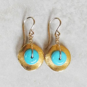 May include: Gold earrings with turquoise stones. The earrings are made of a thin, flat piece of gold metal with a turquoise stone in the center. The earrings are suspended from a gold hook.