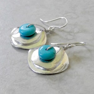 May include: Silver earrings with a layered, organic shape and a turquoise bead accent.