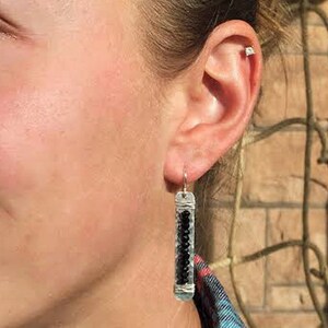 May include: Silver dangle earrings with a black bead design. The earrings are long and narrow, with a silver hook.