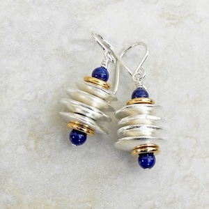 May include: Silver and gold earrings with blue gemstone accents. The earrings feature a stack of layered silver discs with gold accents between each disc.