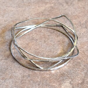 May include: A silver bangle bracelet made of multiple intertwined bands. The bands are hammered and have a slightly irregular shape.