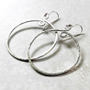 May include: A pair of silver hoop earrings with a hammered finish and a delicate swirl design. The earrings are lightweight and have a simple, elegant style.