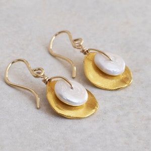 May include: A pair of gold earrings with a white pearl accent. The earrings are made of hammered gold and have a simple, elegant design.