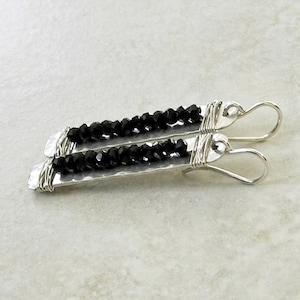 May include: A pair of silver earrings with black beads and hammered metal accents. The earrings have a simple, modern design.