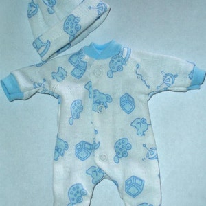 May include: A white baby sleepsuit and matching hat set. The sleepsuit has long sleeves and feet, with blue trim and popper fastenings. Both items are patterned with blue cartoon illustrations.