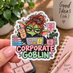 May include: A die-cut sticker featuring a green goblin with messy auburn hair, wearing leopard print glasses, working at a laptop. The sticker includes text: FUELED BY CAFFEINE & CHAOS, SAME SHIT DIFFERENT DAY, HOT MESS EXPRESS, and CORPORATE GOBLIN.