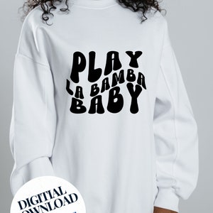 May include: White sweatshirt with black text that reads "Play La Bamba Baby" in a retro font. The text is in a curved shape and is centered on the sweatshirt.