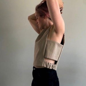 Puede incluir: Un top beige sin mangas con un diseño único de corte. El top es corto y tiene una cintura elástica fruncida.