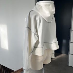 May include: White cropped hoodie with a contrasting stitch detail around the hood, sleeves, and hem.