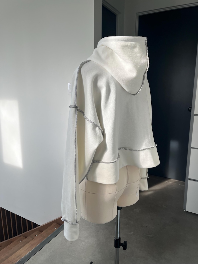 May include: White cropped hoodie with a contrasting stitch detail around the hood, sleeves, and hem.