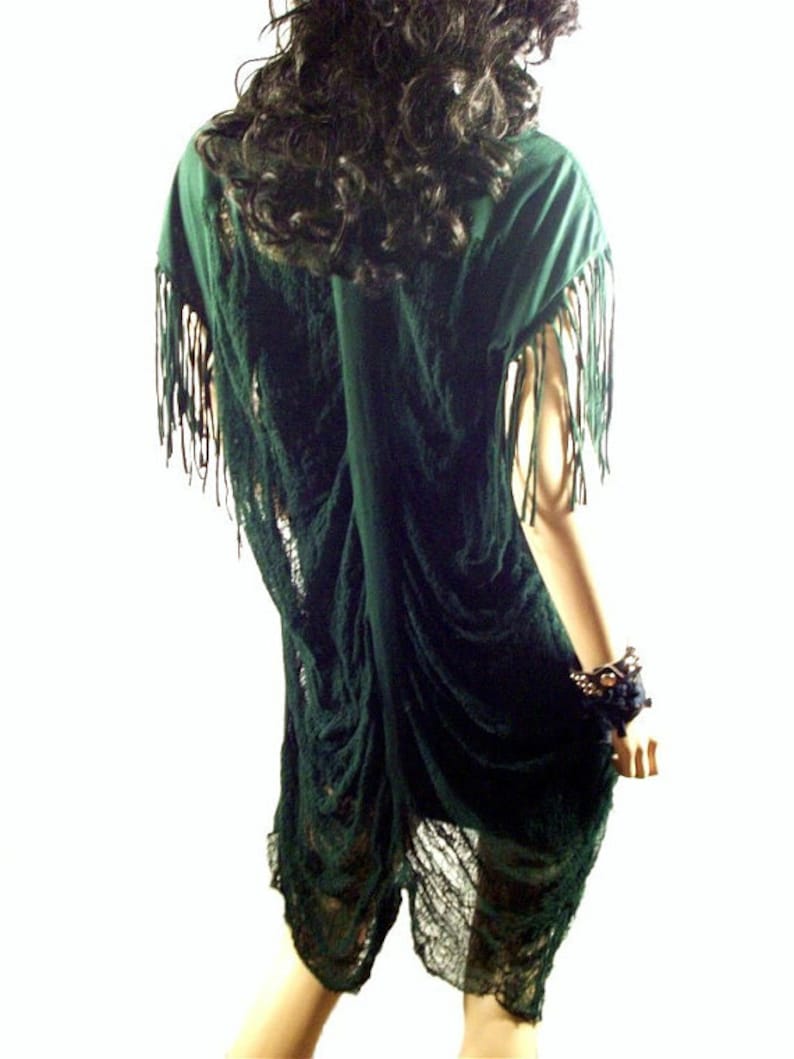May include: A dark green, loose-fitting, fringed dress with a sheer, lace-like overlay. The dress is gathered and draped, creating a flowing, bohemian style.