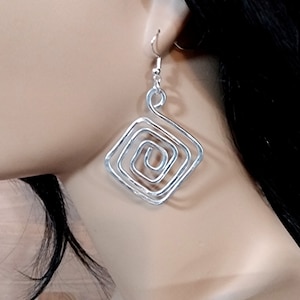 May include: Silver spiral earrings with a square shape. The earrings are made of wire and have a delicate, intricate design.