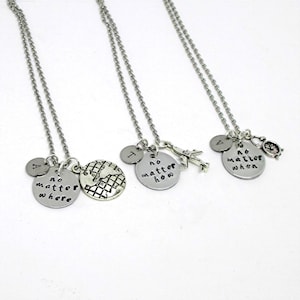 Op de afbeelding: Drie zilveren kettingen met bedels. De eerste ketting heeft een globe-bedel, een bedel met de tekst "no matter where" en een bedel met de letter "A". De tweede ketting heeft een bedel met de tekst "no matter how", een bedel met de letter "I" en een bedel van een vliegtuig. De derde ketting heeft een bedel met de tekst "no matter when", een bedel met de letter "V" en een bedel van een klok.