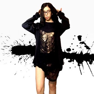 K&ouml;nnte beinhalten: Eine Person tr&auml;gt ein schwarzes Langarmshirt mit einem abgenutzten Design. Das Shirt hat ein gro&szlig;es Loch vorne und ist teilweise durchsichtig. Die Person tr&auml;gt eine Brille und hat lange dunkle Haare.