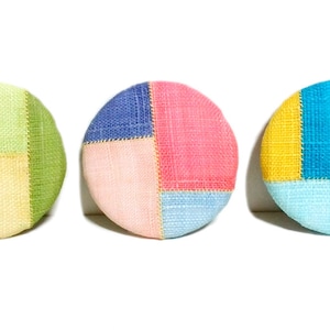 Peut inclure: Trois boutons ronds en tissu avec un motif patchwork. Les boutons sont faits de différentes couleurs et textures, notamment du vert, du jaune, du bleu, du rose et du blanc.