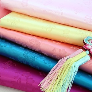 Peut inclure: Cinq échantillons de tissu colorés empilés avec un motif floral. Le tissu est lisse et soyeux. Un charme papillon bleu et rose avec un pompon pend du haut de la pile.