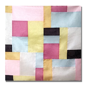 May include: A square patchwork textile with a variety of colours and patterns. The design includes rectangular and square shapes in pink, yellow, light blue, white, and black. The fabric has a subtle sheen, suggesting a silk or satin material.