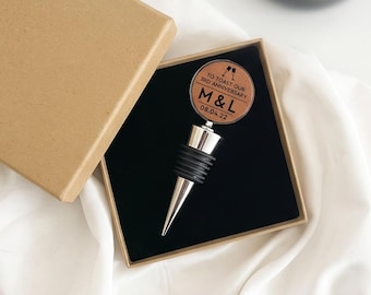 May include: A silver-toned metal bottle stopper with a circular wooden top featuring the engraved text TO TOAST OUR 3RD ANNIVERSARY M&L 08.04.22 and a graphic of two glasses. The stopper is presented in a square cardboard gift box with a black insert.