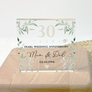 May include: A wooden block with a clear acrylic panel featuring text and floral accents. The panel reads "30 YEARS PEARL WEDDING ANNIVERSARY Mum & Dad 02.10.1994" in elegant script and font. The design includes green leaves.