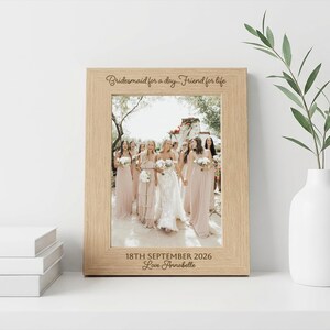 May include: A light wood picture frame containing a photograph of a wedding party. The top of the frame is engraved with "Bridesmaid for a day... Friend for life" and the bottom is engraved with "18TH SEPTEMBER 2026" and "Love Annabelle".