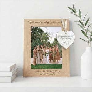 May include: A light wood picture frame featuring the engraved text "Bridesmaid for a day... Friend for life" at the top and "18TH SEPTEMBER 2026 Love Annabelle" at the bottom, with a white heart-shaped ceramic ornament hanging from the frame.