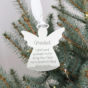 May include: A silver angel-shaped Christmas ornament with the word "Grandad" and a sentimental message engraved on it. The ornament hangs from a white ribbon against a backdrop of a Christmas tree.