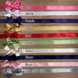 May include: Assortment of satin ribbon spools in various colors, including pink, white, purple, gold, red, green, ivory, navy, blush, and silver/grey. Each spool has a matching bow tied on top.