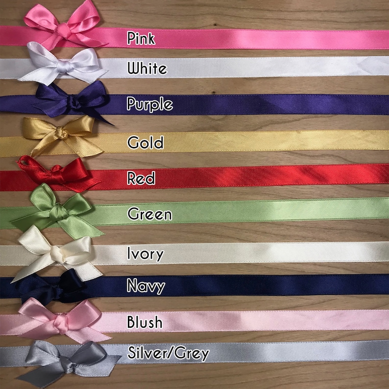 May include: Assortment of satin ribbon spools in various colors, including pink, white, purple, gold, red, green, ivory, navy, blush, and silver/grey. Each spool has a matching bow tied on top.