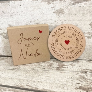 May include: A wooden box with the names "James and Nicola" engraved on it. A round wooden plaque with a red heart in the centre and the text "525600 Minutes - 52 Weeks - 365 Days - 8760 Hours - 12 Months - 1556952 Seconds - 1 Year" engraved around it.