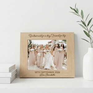 May include: A light wood picture frame containing a photograph of a wedding party. The top border is engraved with "Bridesmaid for a day... Friend for life" and the bottom border features "18TH SEPTEMBER 2026" and "Love Annabelle" in script.