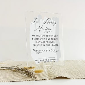 May include: A clear acrylic sign with a grey watercolour design and the text "In Loving Memory" in black cursive. The sign also includes the text "Of those who cannot be here with us today, but are forever present in our hearts today and always." and "Thomas and Jessica 25th June 2024".