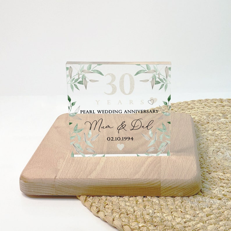 May include: A wooden block with a clear acrylic panel featuring text and floral accents. The panel reads "30 YEARS PEARL WEDDING ANNIVERSARY Mum & Dad 02.10.1994" in elegant script and font. The design includes green leaves.