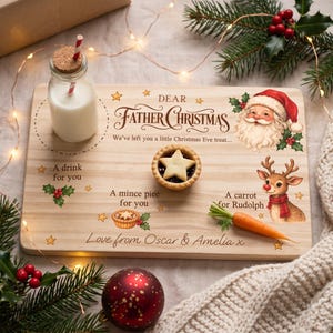 May include: A rectangular wooden serving board featuring the text Dear Father Christmas, We've left you a little Christmas Eve treat, A drink for you, A mince piee for you, A carrot for Rudolph, and Love from Oscar & Amelia x, with illustrations of Santa, a reindeer, holly, and stars.