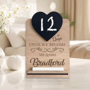 May include: A wooden countdown sign with a chalkboard heart that says "12" and the text "Days Until We Become Mr & Mrs Bradford".