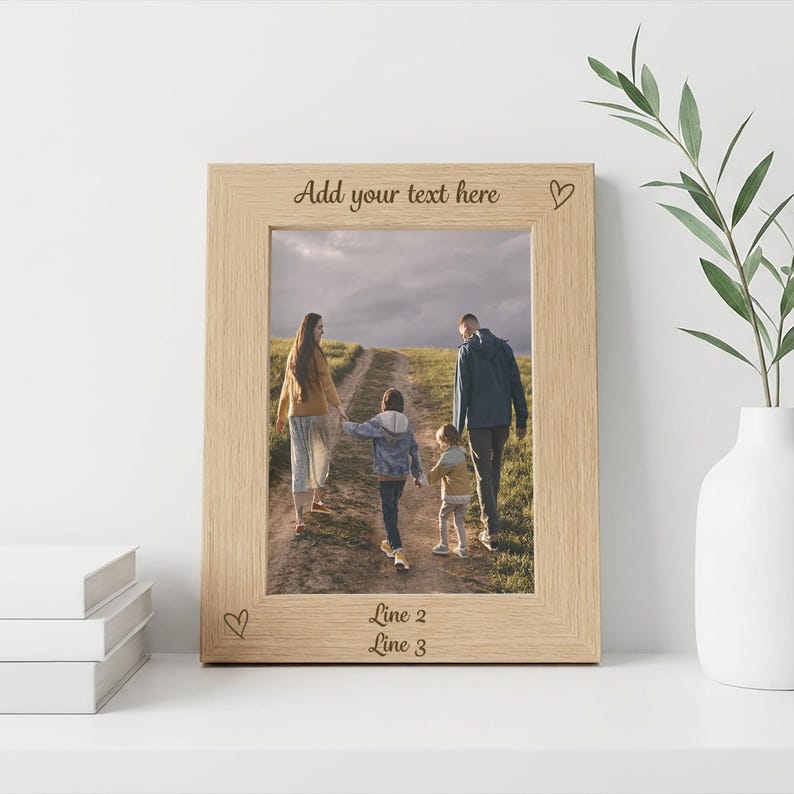 May include: A light-colored wooden picture frame with a family photo inside. The frame has the text "Add your text here" at the top and "Line 2" and "Line 3" at the bottom. Small heart symbols are etched on the frame.